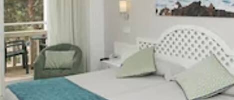 A hotel room with a bed, a window with curtains, a painting on the wall, and a chair outside the window.