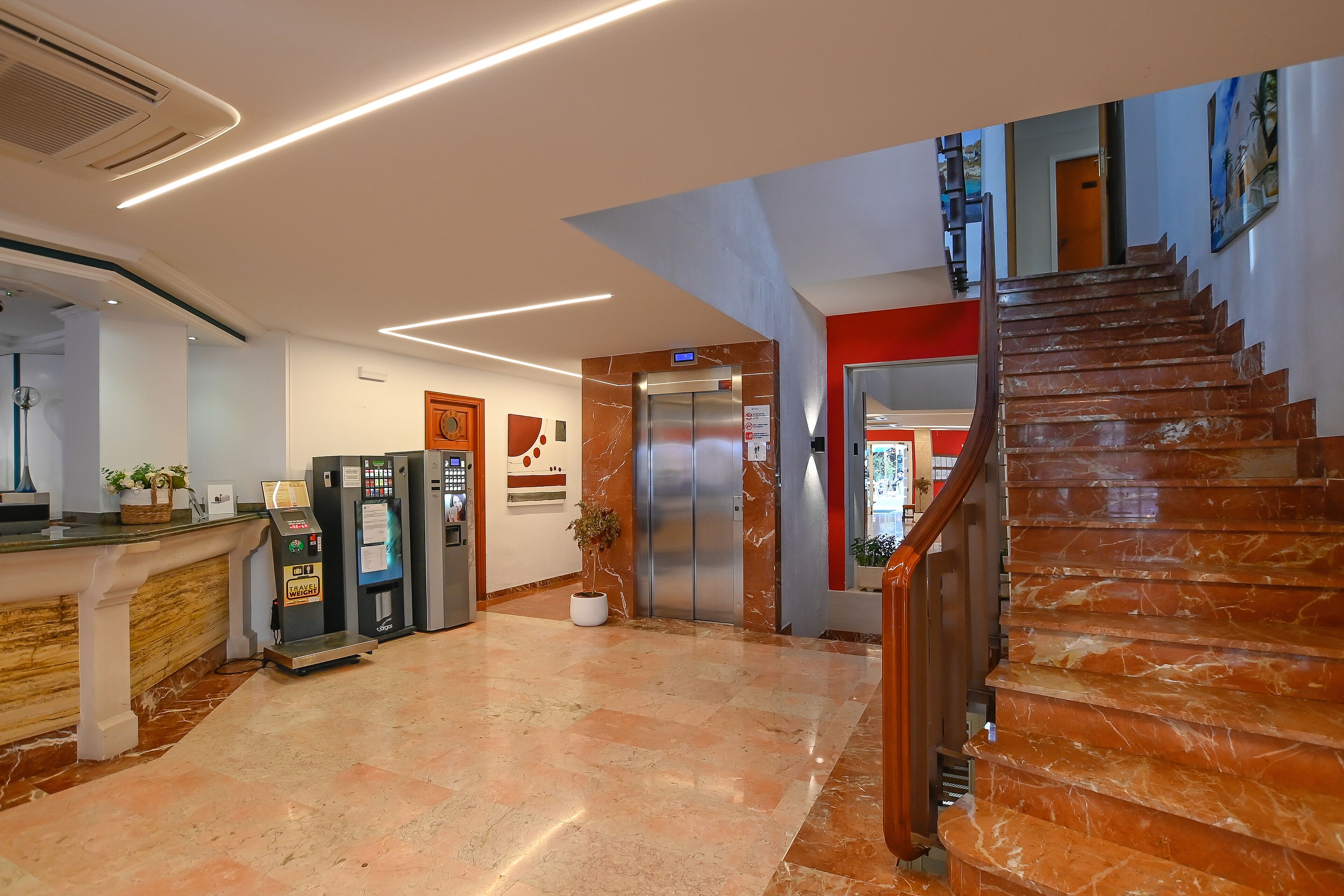 A hotel lobby with a marble staircase, an elevator, and a reception desk.