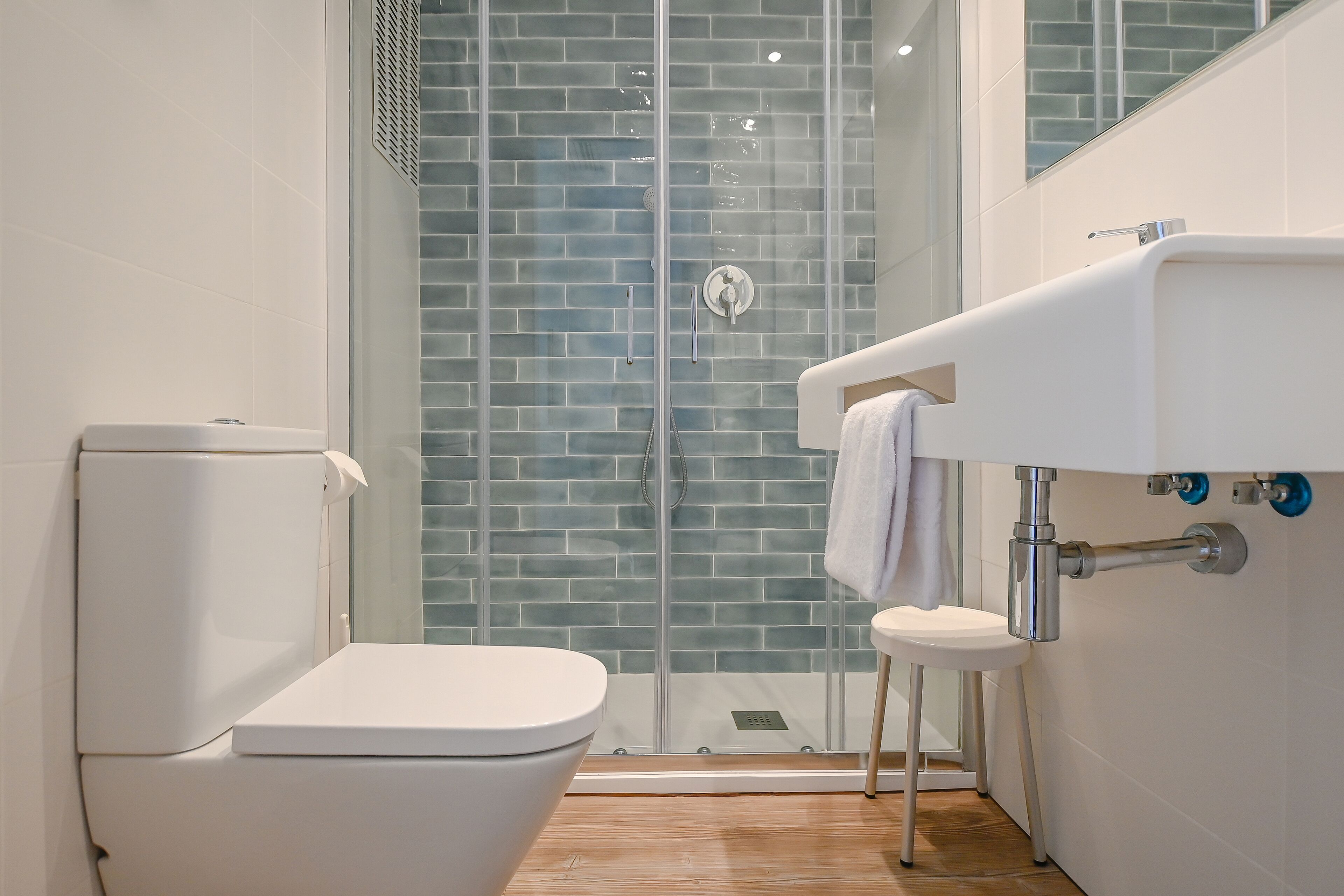 A modern bathroom with a glass shower enclosure, a white toilet, and a sink with a towel hanging on the wall.