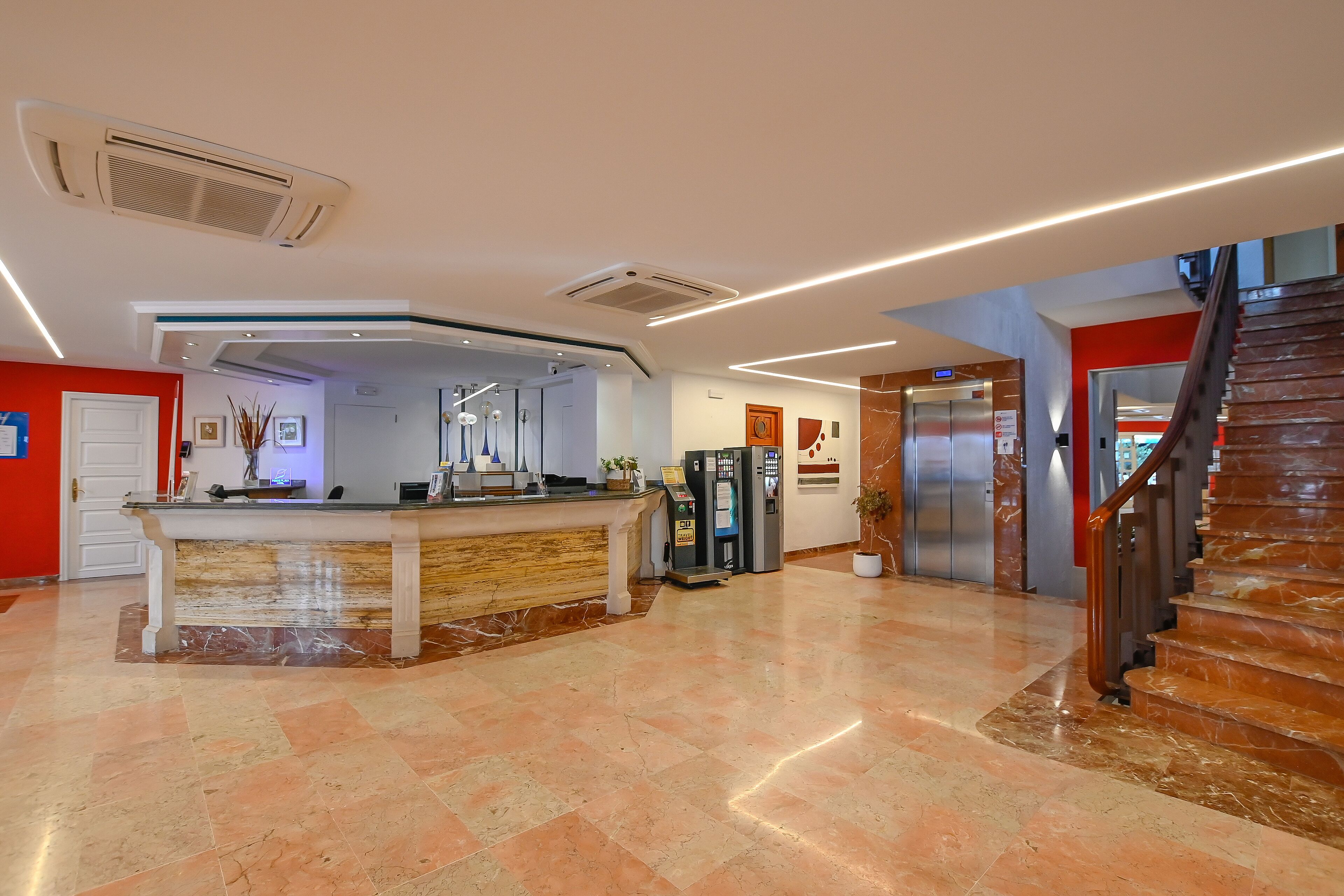 A hotel lobby with a reception desk, a staircase, and an elevator.