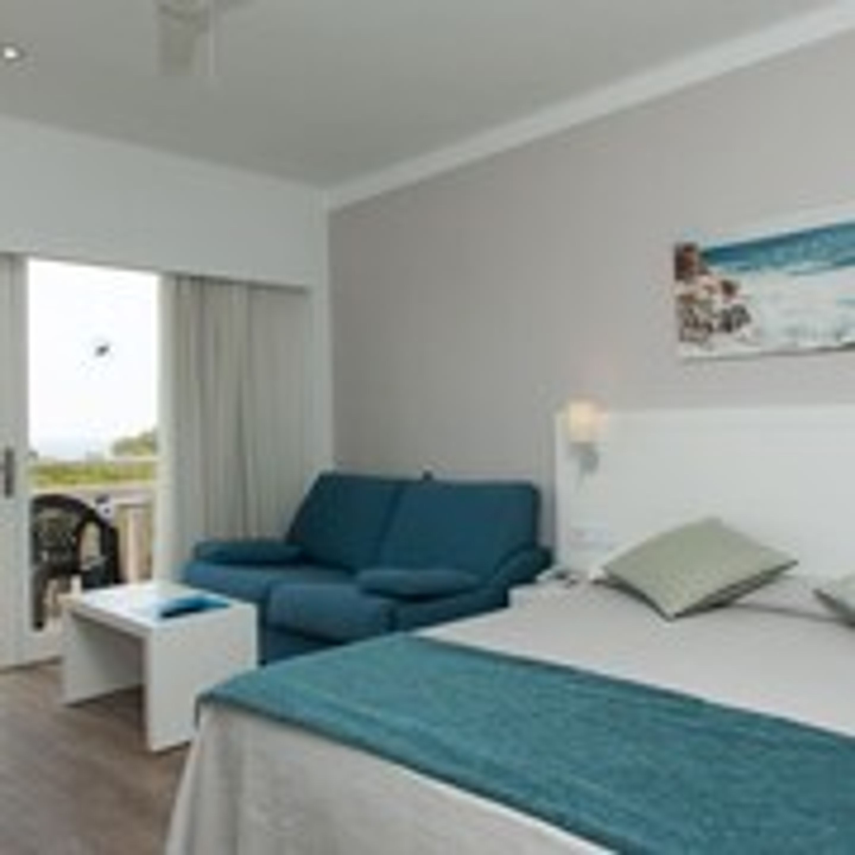 Ein Hotelzimmer mit einem Bett, einem blauen Sofa, einem kleinen Tisch und einem Fenster mit Vorhängen.