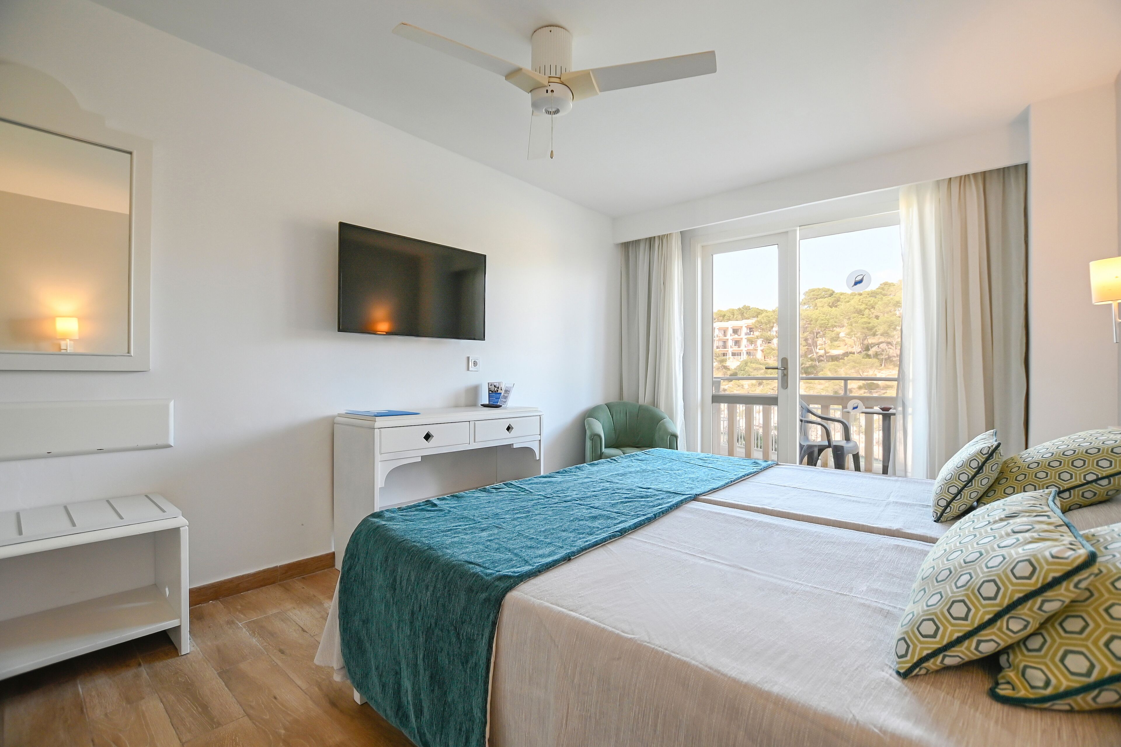 Habitación de hotel con cama, escritorio, silla, televisor y balcón con vistas.