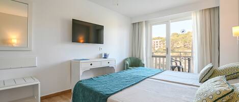 Habitación de hotel con cama, escritorio, silla, televisor y balcón con vistas.