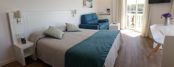 Ein modernes Hotelzimmer mit einem Bett, einem blauen Sessel, einem kleinen Tisch und einem Fernseher an der Wand.
