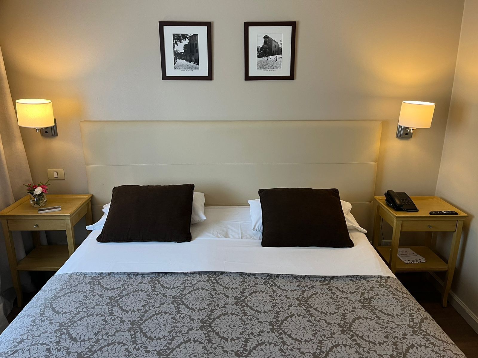A hotel room with a bed, two nightstands, a lamp on each side, and two framed pictures on the wall.