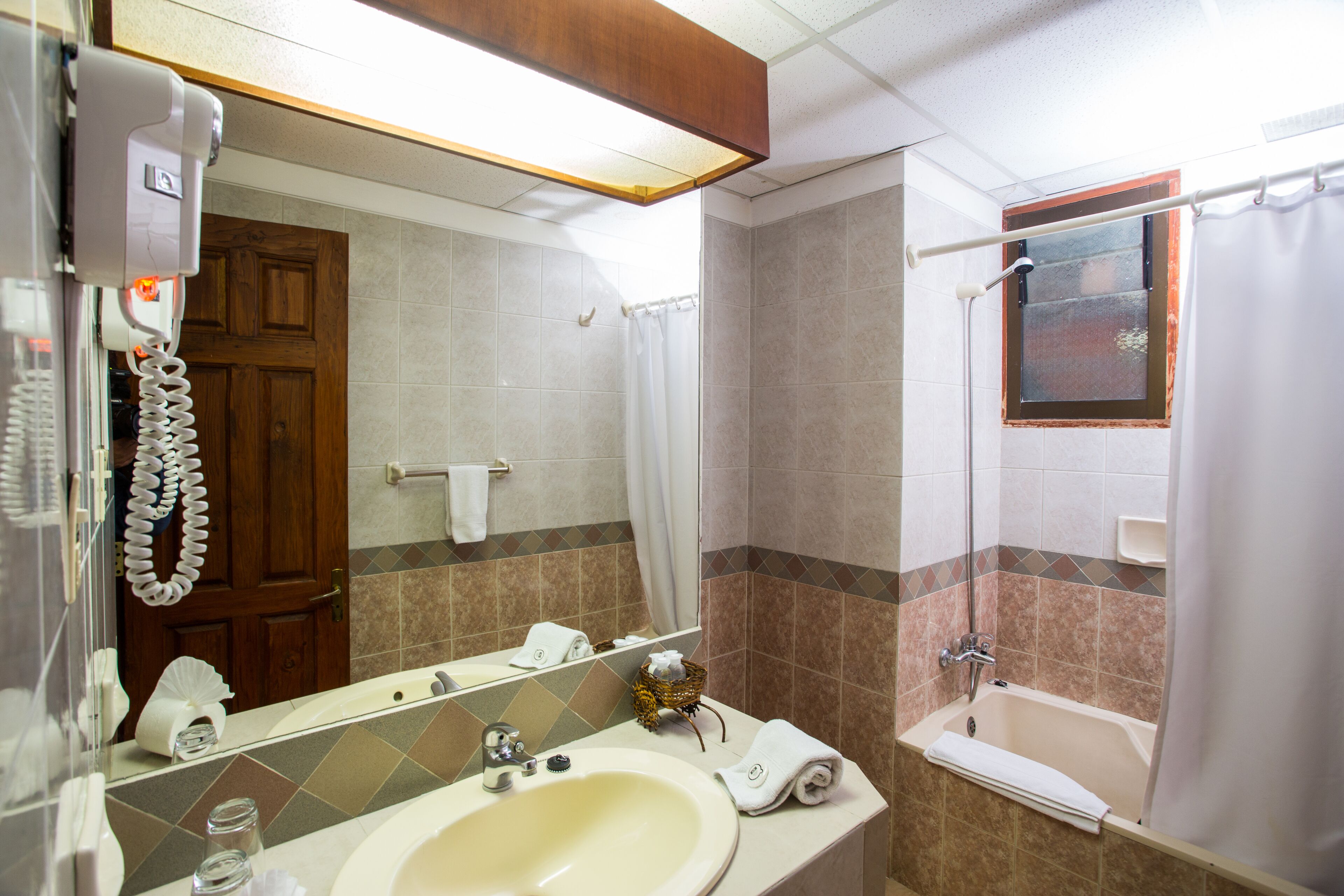 A bathroom with a sink, mirror, shower, and a telephone.
