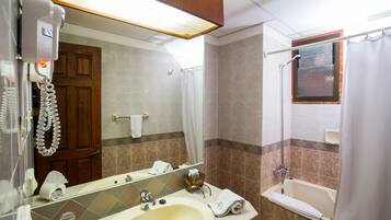A bathroom with a sink, mirror, shower, and a telephone.