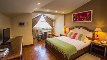 A hotel room with a bed, bedside tables, a desk with a TV, a chair, and a window with curtains.