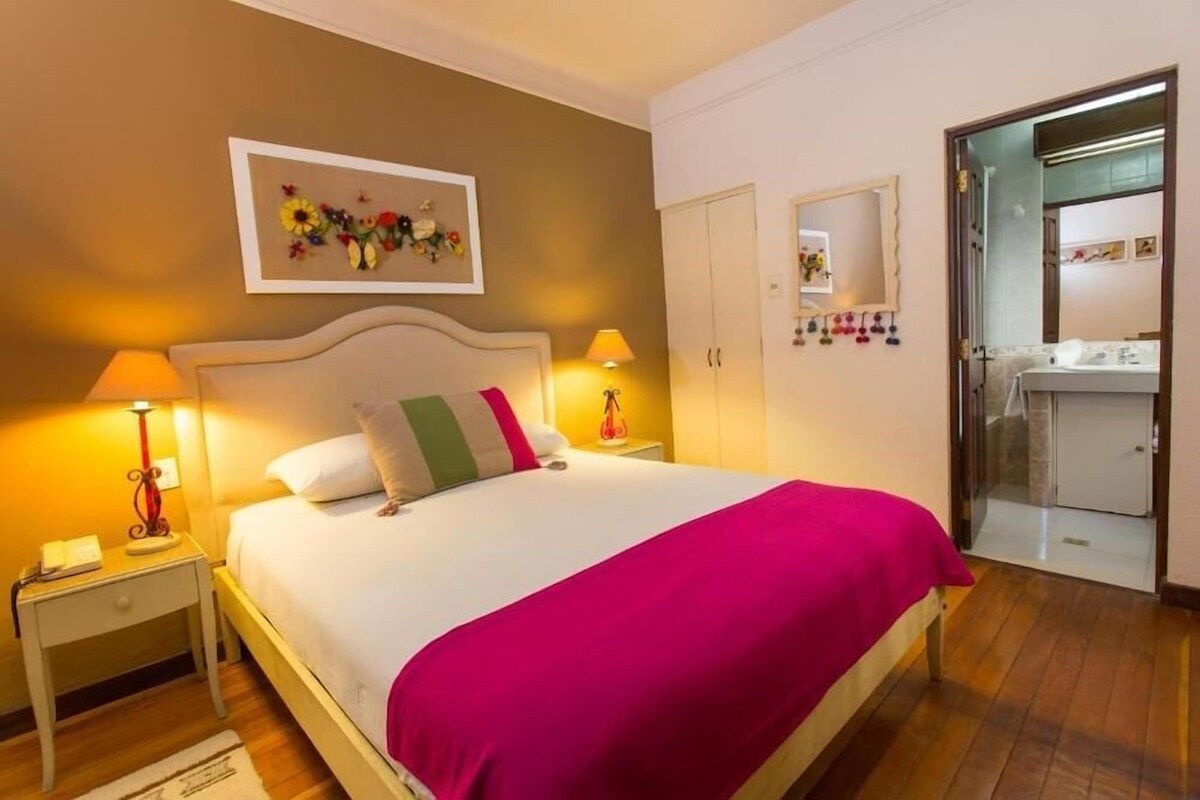 Une chambre d’hôtel avec un lit, des lampes de chevet, une table de nuit, une armoire et une salle de bain visible à travers une porte ouverte.