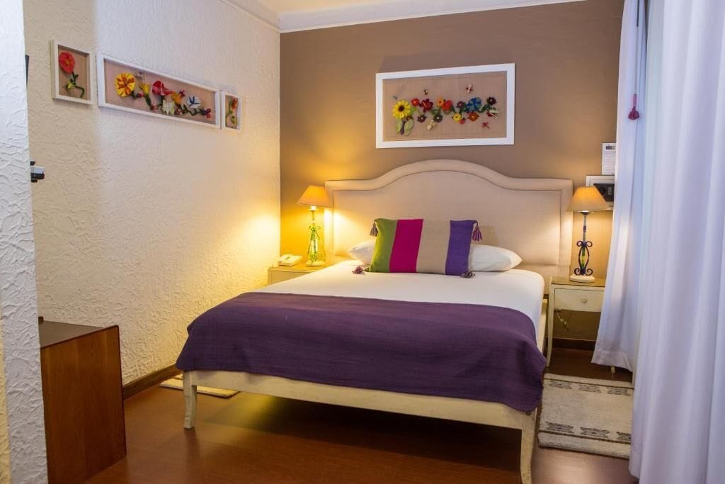 Un dormitorio ordenado con una cama, dos mesitas de noche, una lámpara y una obra de arte floral enmarcada en la pared.
