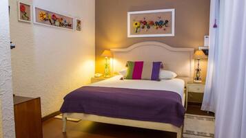 Un dormitorio ordenado con una cama, dos mesitas de noche, una lámpara y una obra de arte floral enmarcada en la pared.