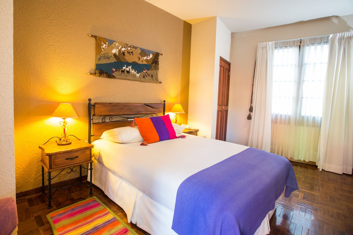 A neatly made bed with a blue blanket, two bedside lamps, and a colorful rug.