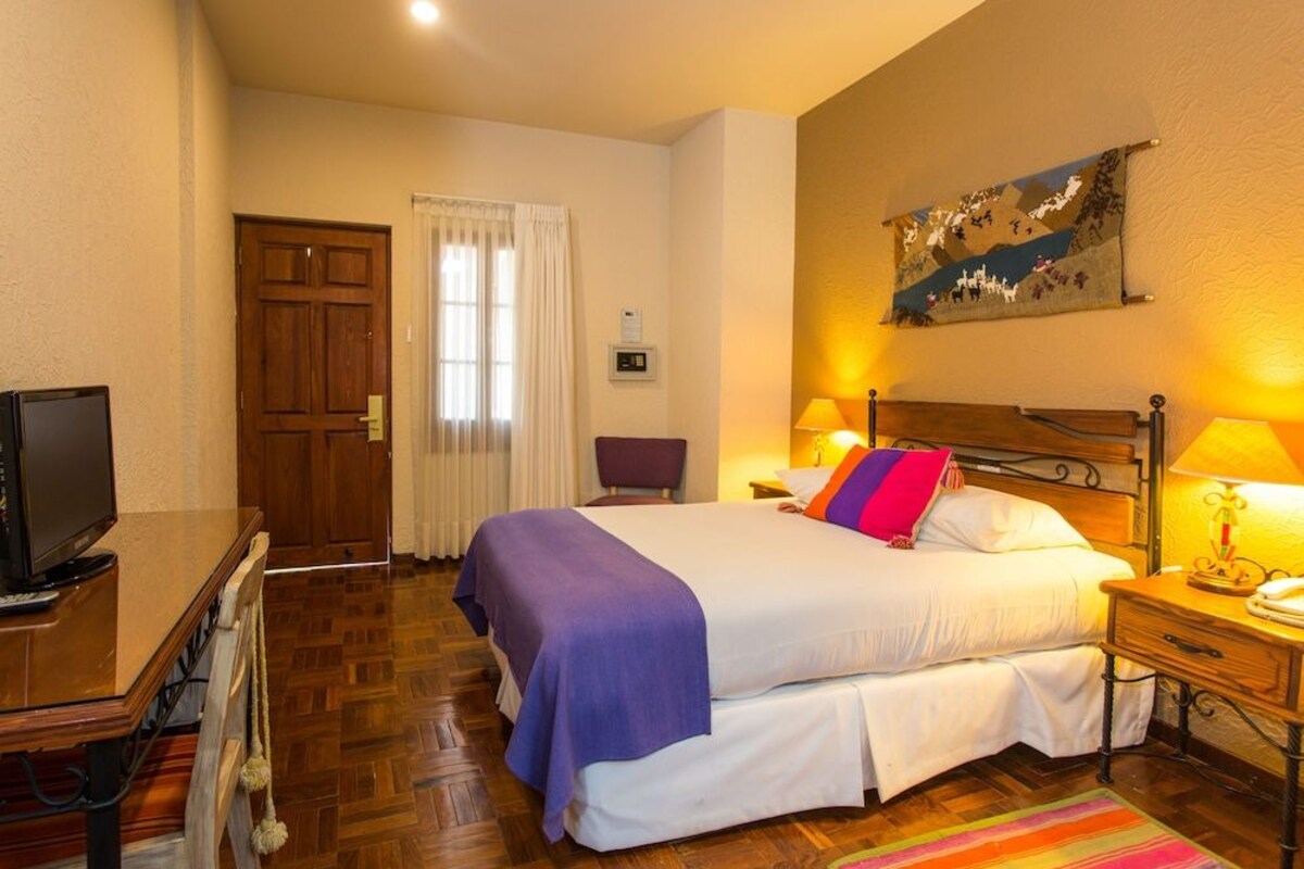 Une chambre d’hôtel avec un lit, une télévision, un bureau, une chaise et un tableau au mur.