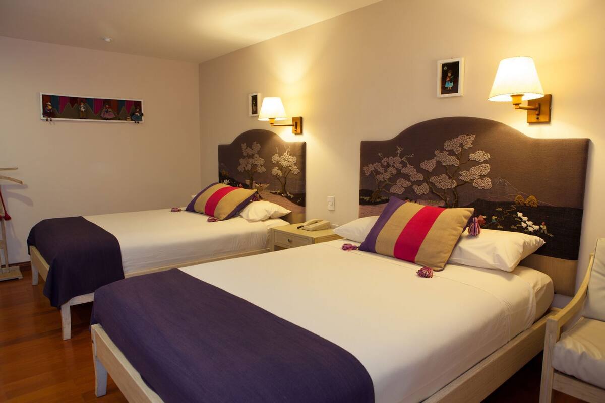 A hotel room with two beds, each with a headboard, bedside tables, and lamps.