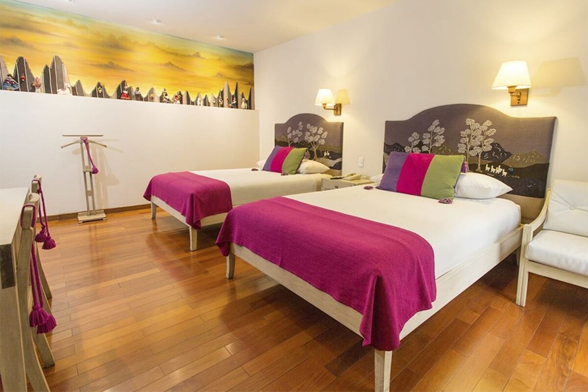 Une chambre d’hôtel avec deux lits, un plancher en bois, un tableau au mur et des lampes fixées au mur.