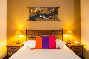 Una habitación de hotel con una cama, dos mesitas de noche, una lámpara, un teléfono y un cuadro en la pared.