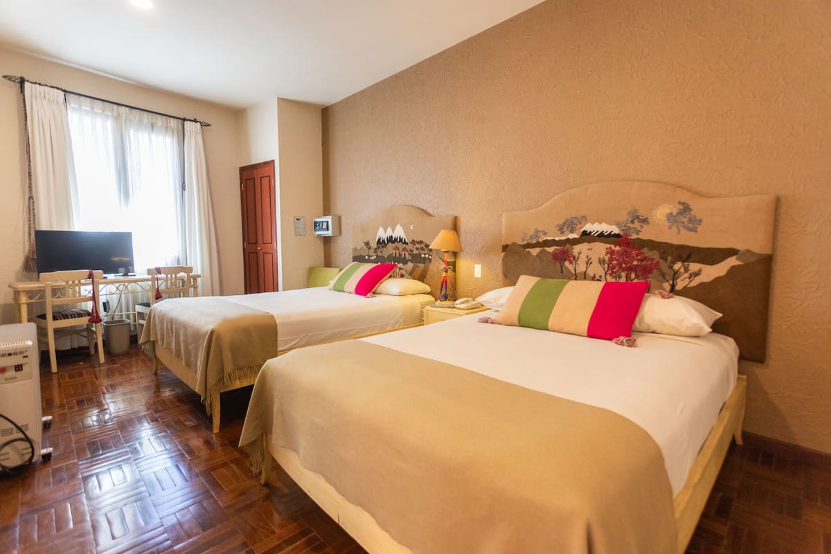 A hotel room with two beds, a desk with a television, and a window with curtains.