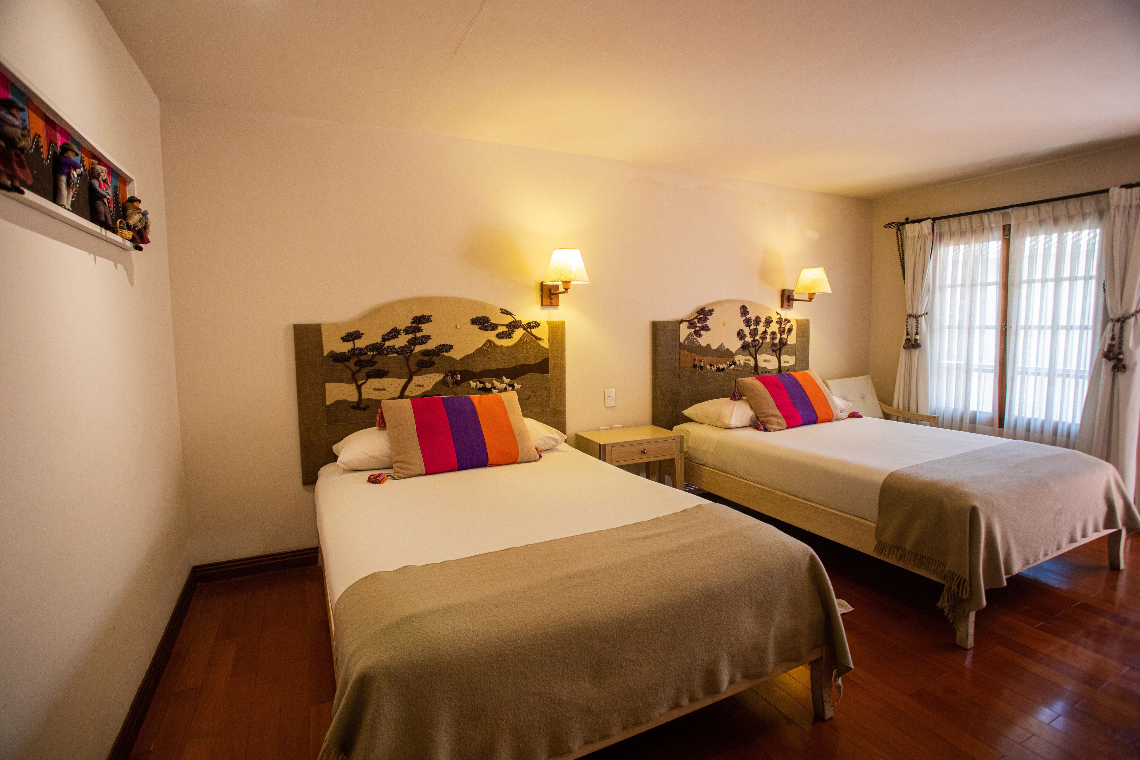 A hotel room with two single beds, each with a headboard, bedside lamps, and a small nightstand.
