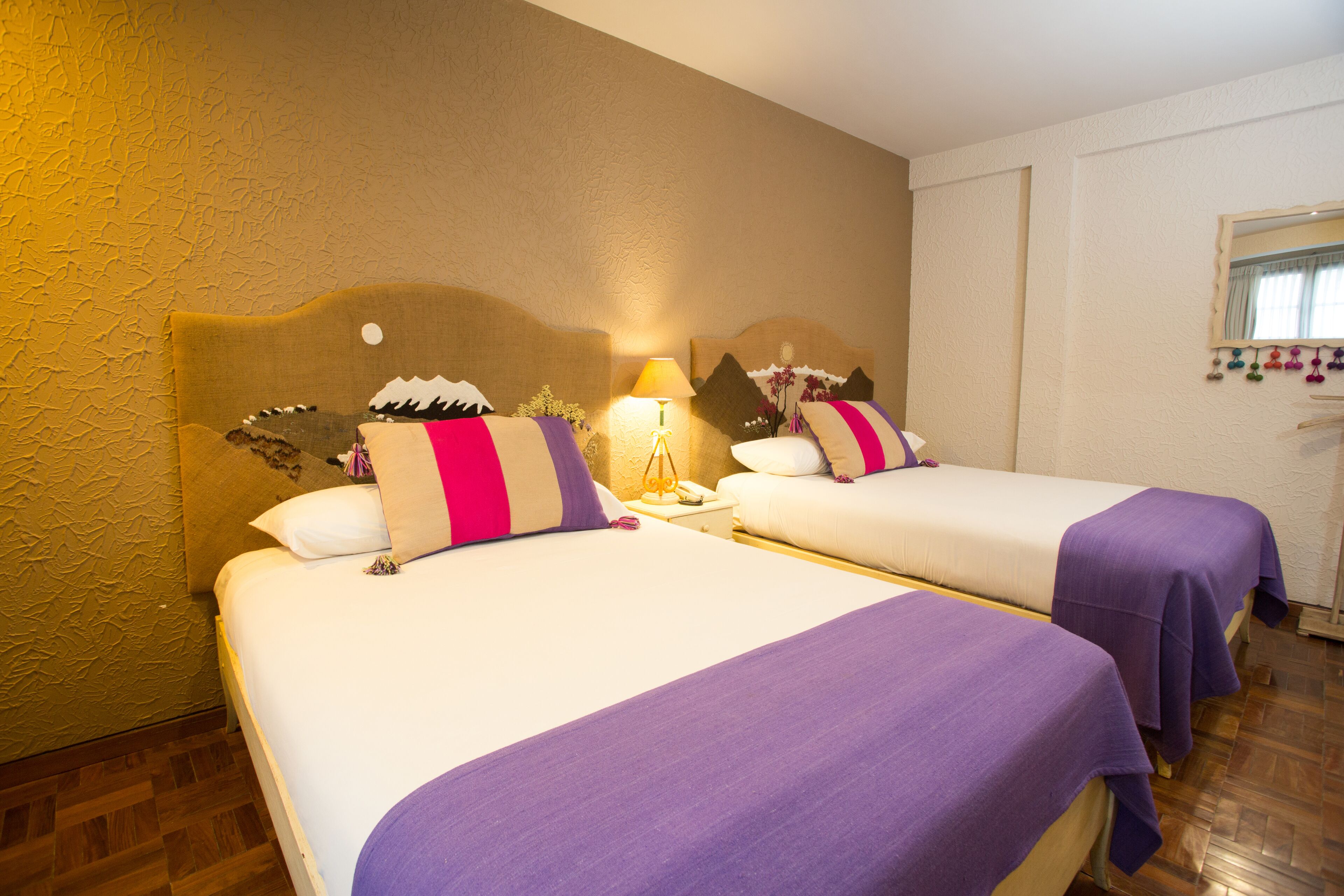 A hotel room with two beds, each with a headboard, a nightstand, and a lamp.