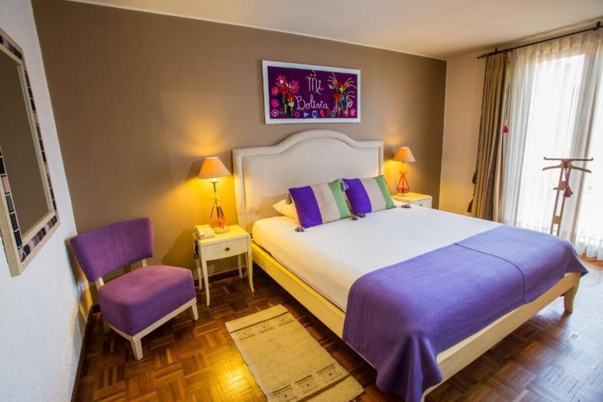 A bedroom with a bed, two bedside tables, a chair, a wall art piece, and a window with curtains.