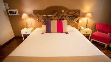 Une chambre d’hôtel avec un grand lit, deux tables de chevet, une chaise rouge et une tête de lit décorative.