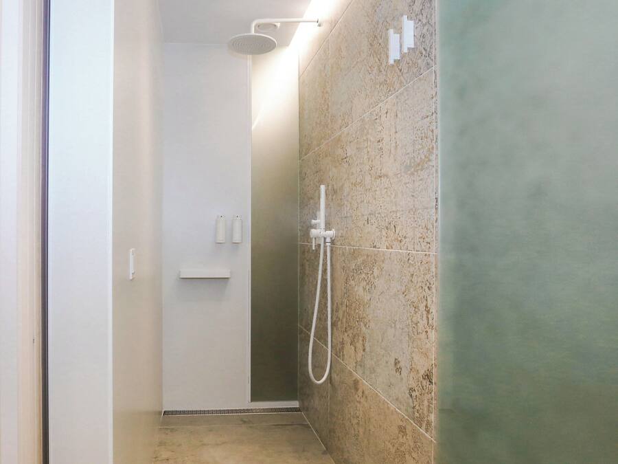 Un baño moderno con ducha, paredes de azulejos y un estante pequeño.