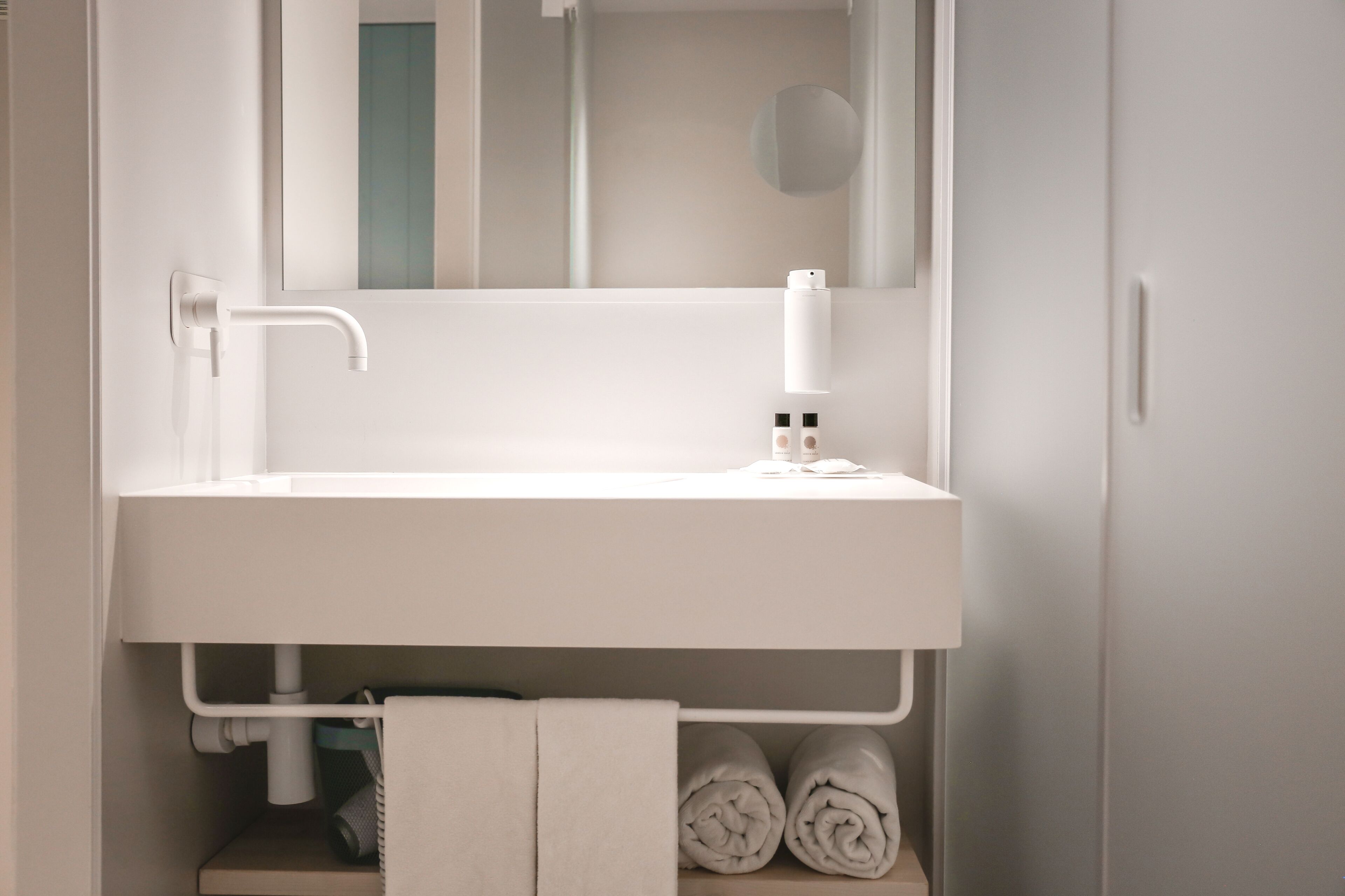 A modern bathroom with a white sink, a mirror, and a towel rack.