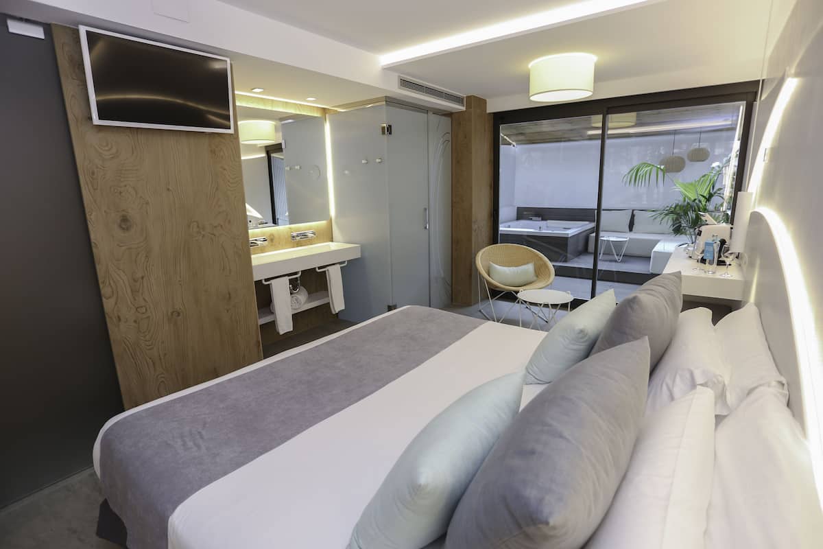 Une chambre d’hôtel moderne dotée d’un grand lit, d’une coiffeuse avec miroir, d’un petit coin salon et offrant une vue sur l’extérieur.