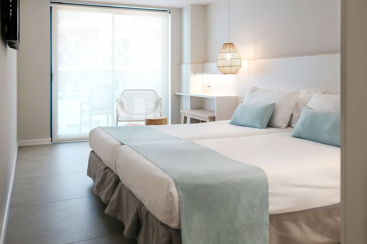 Une chambre d’hôtel moderne dotée d’un grand lit, d’un coin salon avec un fauteuil, une petite table et une lampe fixée au mur.
