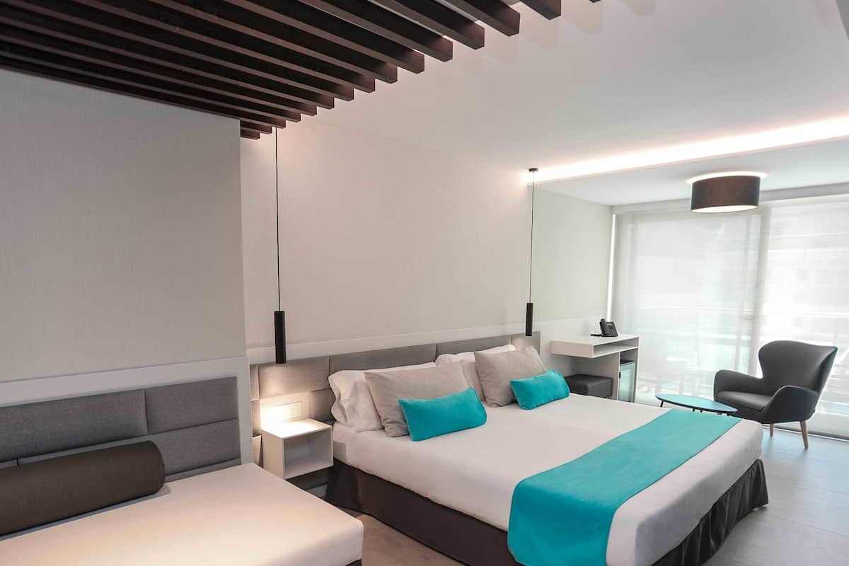 Une chambre d’hôtel moderne, dotée d’un grand lit, d’une table de chevet, d’une chaise et d’un bureau avec une lampe.