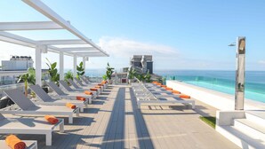 Un área de lounge en la azotea con tumbonas y vista a la piscina.