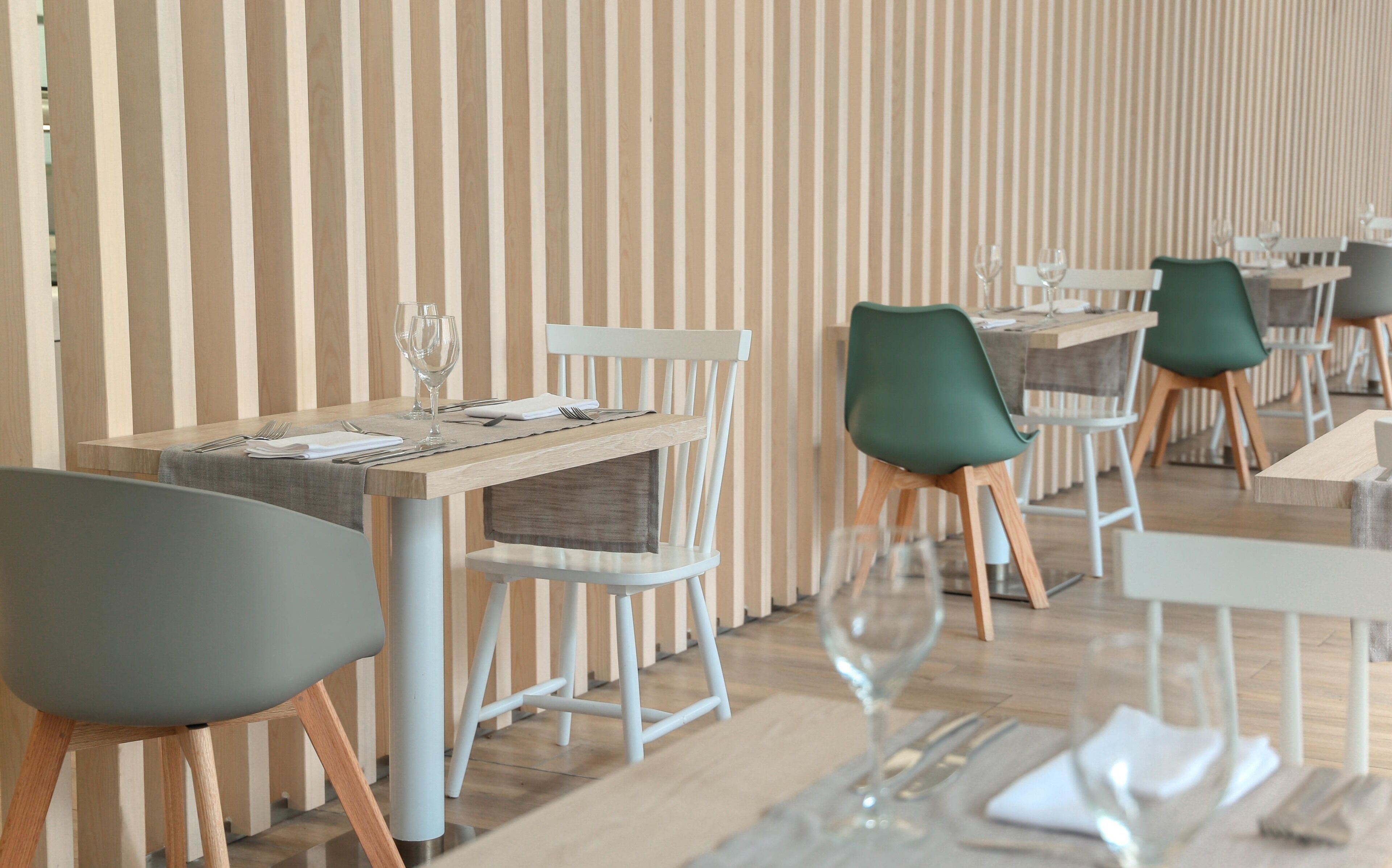 Un interior de restaurante moderno con mesas de madera, sillas verdes y papel tapiz a rayas.