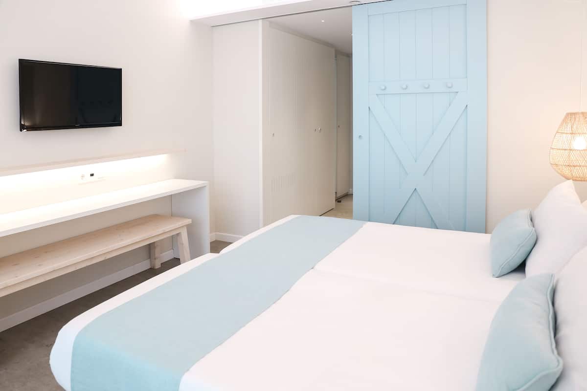 Une chambre à coucher avec un lit, un téléviseur fixé au mur, un banc et une armoire.