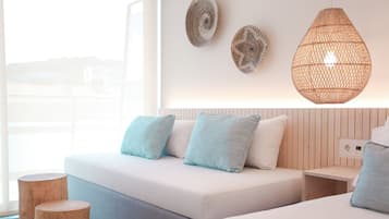 Una habitación de hotel moderna con una cama grande, un sofá más pequeño y un taburete de madera. Se observan adornos en la pared y una lámpara colgante tejida de gran tamaño.