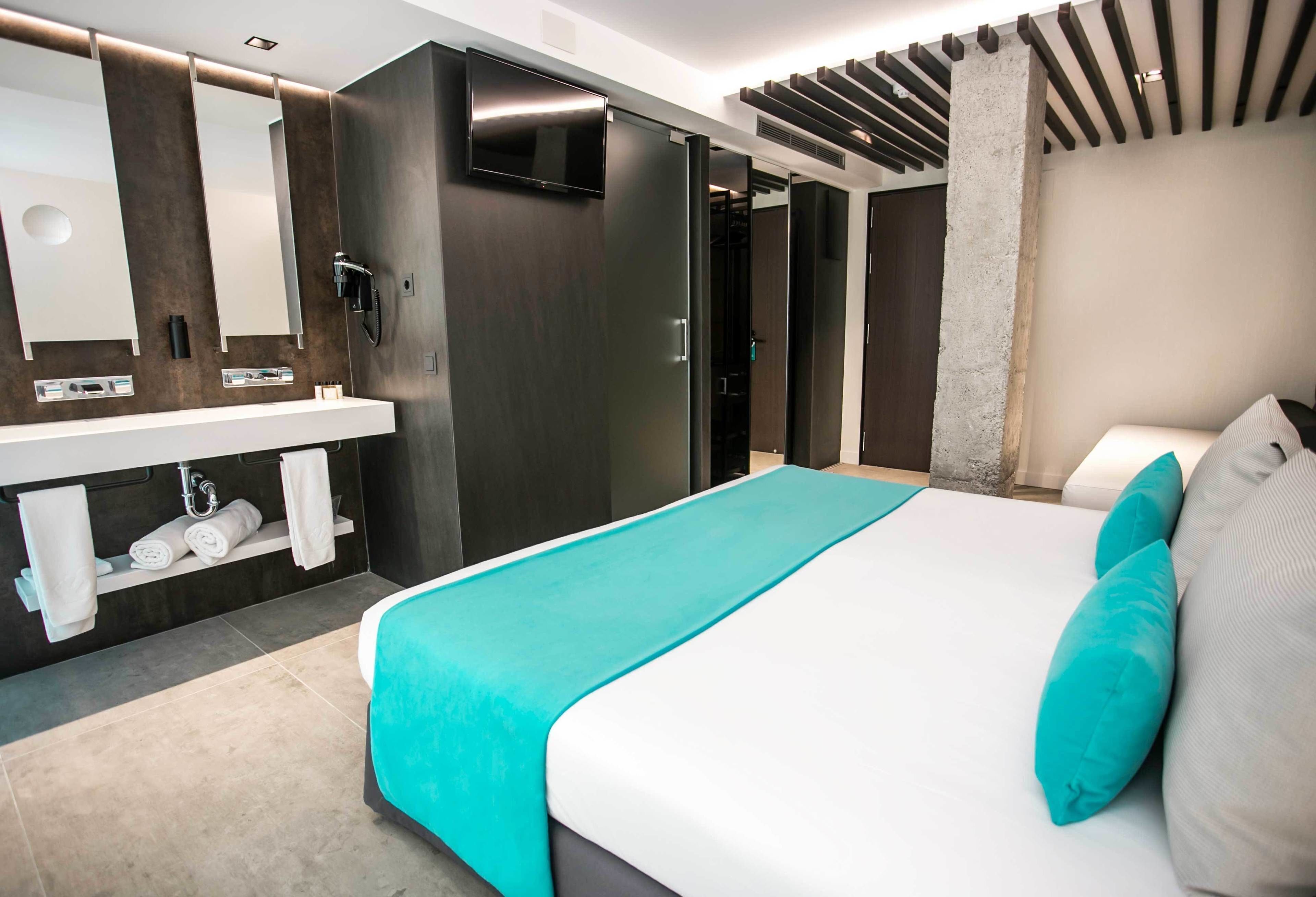A modern hotel room with a large bed, a built-in TV, a bathroom with a vanity, and a shower area.