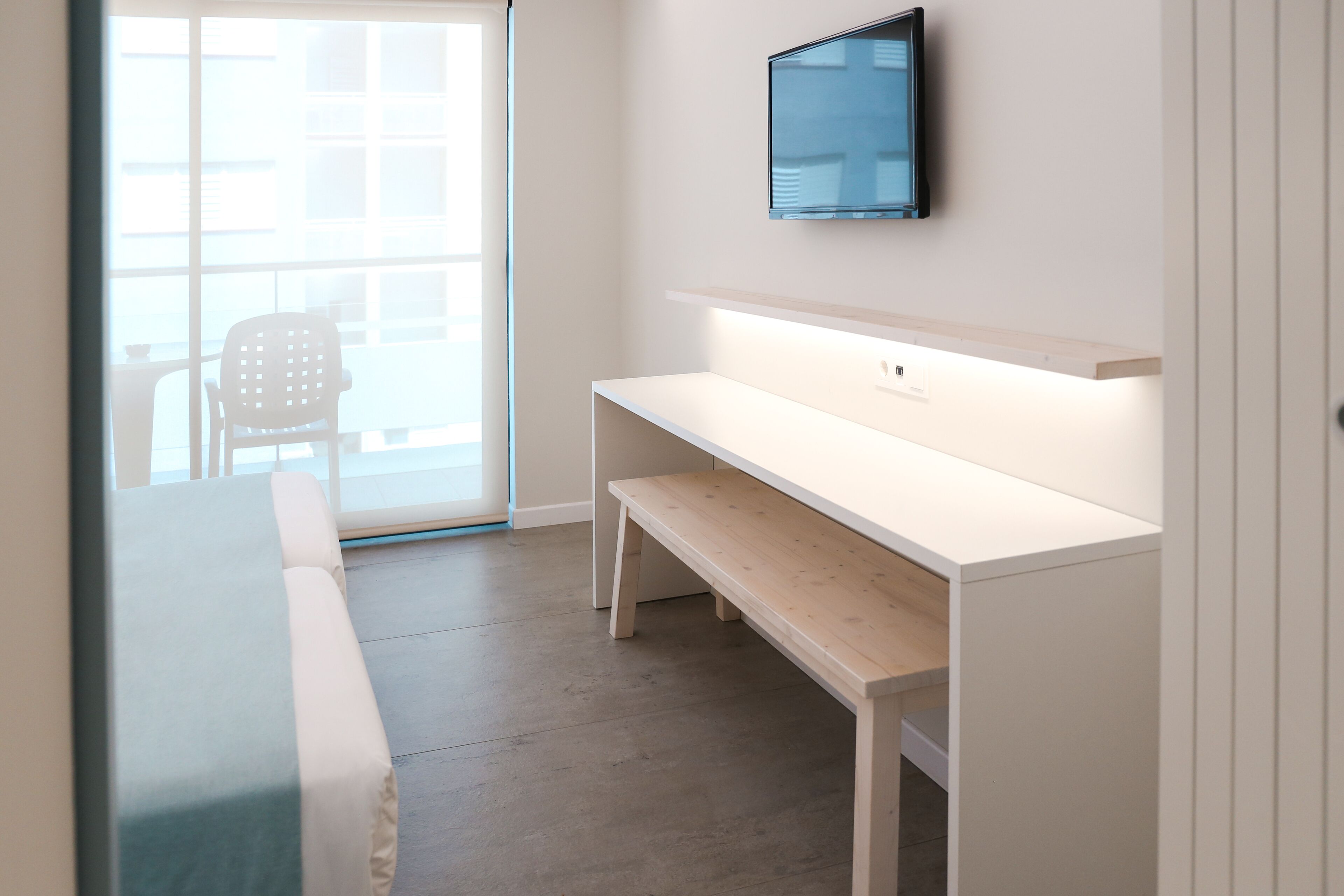 Une chambre moderne avec un bureau blanc, un banc et un téléviseur fixé au mur.