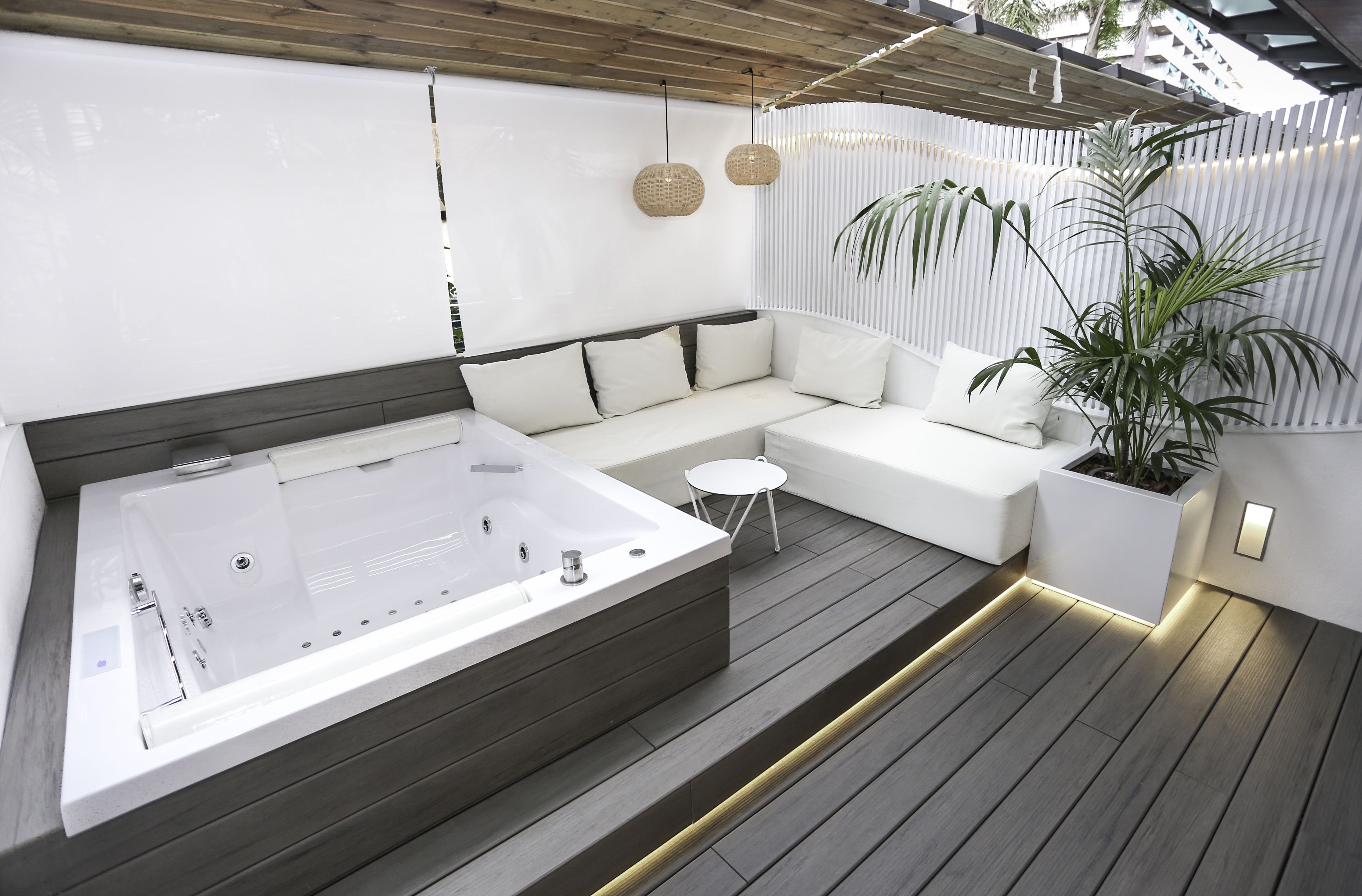 Ein moderner Außenbereich mit Whirlpool, einem weißen Sofa und einem kleinen Tisch.