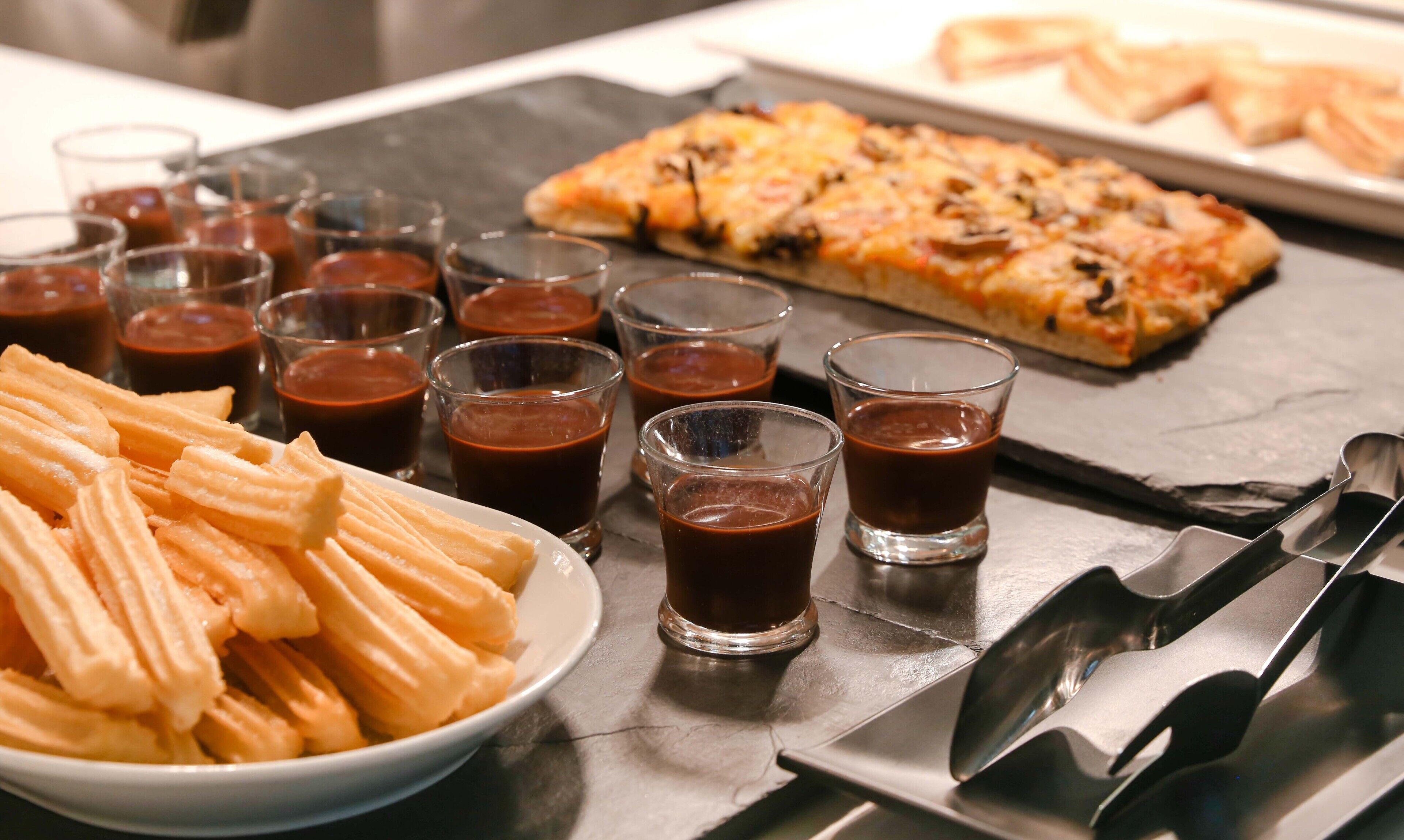 Un plat de xurros, una safata de pizza i diversos vasos de salsa de xocolata.