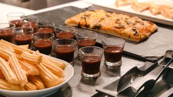 Un plat de xurros, una safata de pizza i diversos vasos de salsa de xocolata.