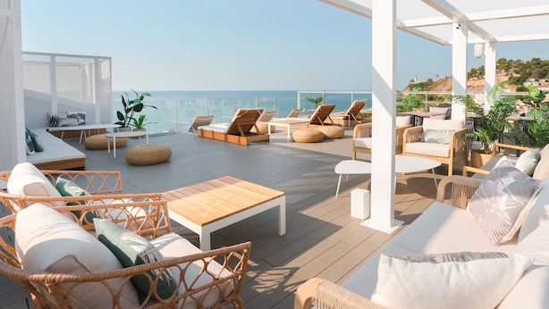 Una terraza en la azotea con mobiliario de mimbre, una mesa de madera y vistas al mar.