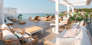A rooftop terrace with wicker furniture, a wooden table, and a view of the sea. - KAKTUS Hotel Kaktus Playa (Calella)
