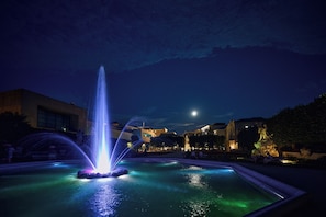 A nighttime fountain with water jets, surrounded by a pool, with buildings and a moon in the background. - Holiday Inn Salzburg City by IHG (Salzburg)