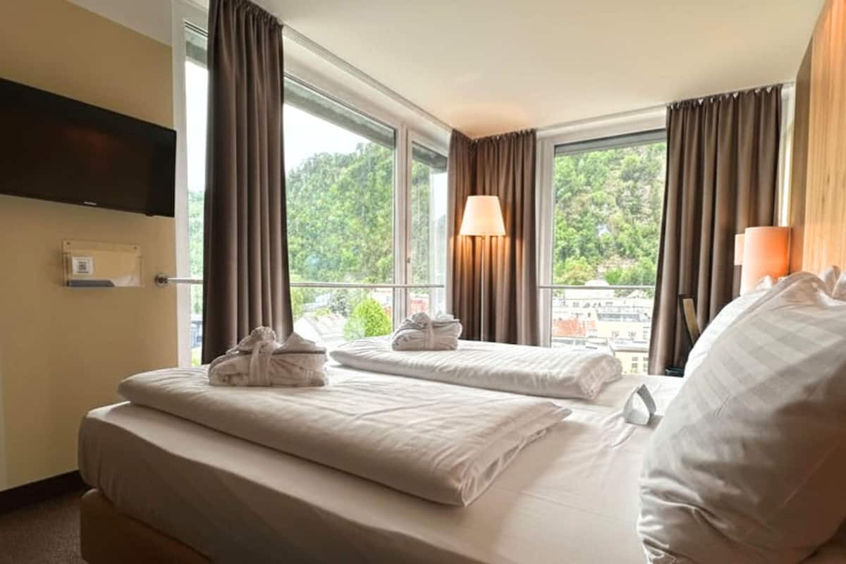 A hotel room with two beds, a TV mounted on the wall, and a window with curtains.