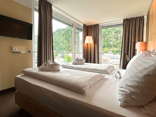 A hotel room with two beds, a TV mounted on the wall, and a window with curtains. - Holiday Inn Salzburg City by IHG (Salzburg)