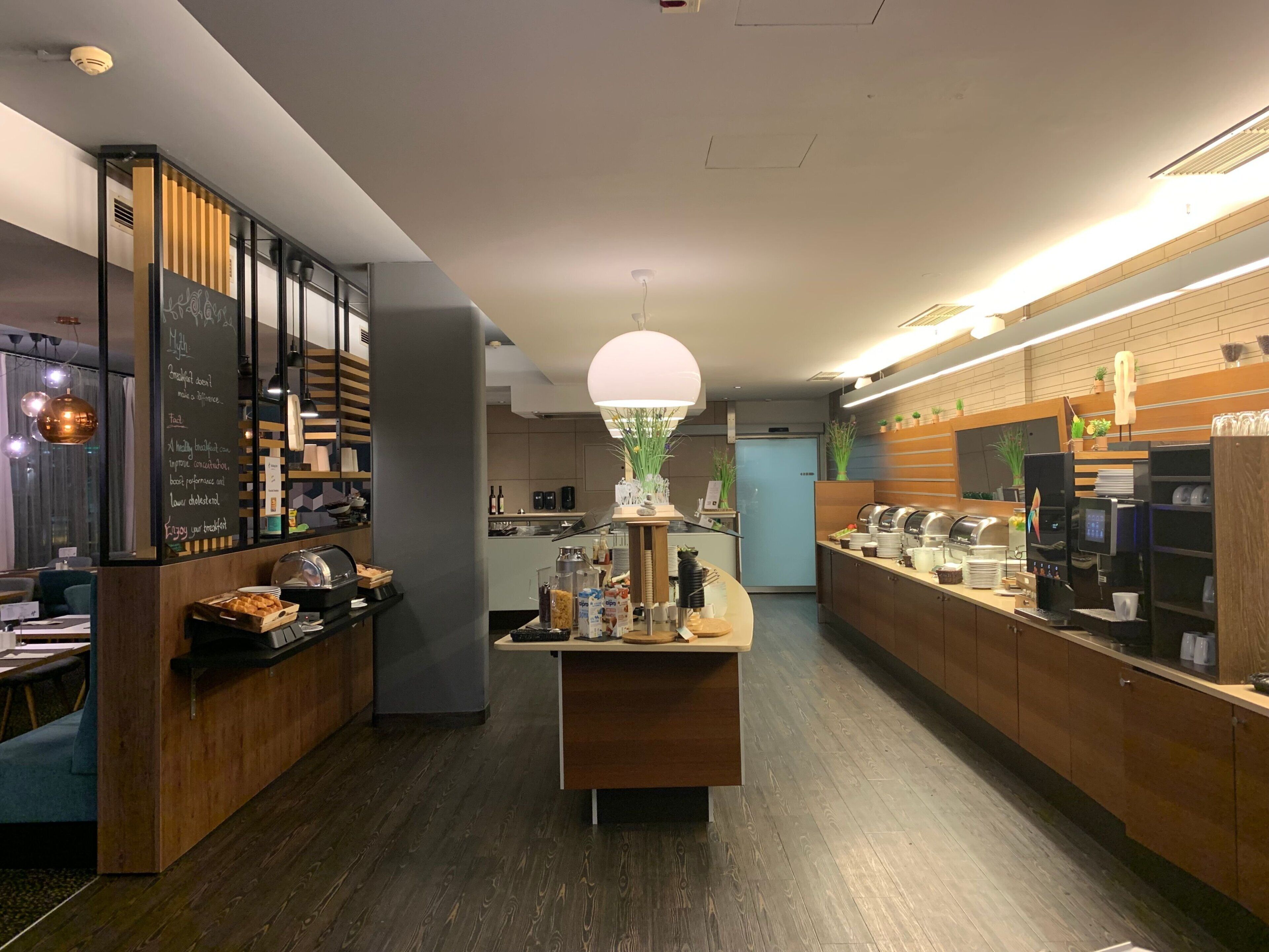 A modern cafe interior with a central serving counter, wooden accents, and a bright pendant light.