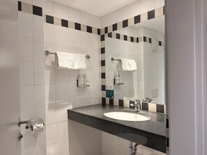 A bathroom with a white sink, a mirror, and two white towels hanging on towel bars. - Holiday Inn Salzburg City by IHG (Salzburg)