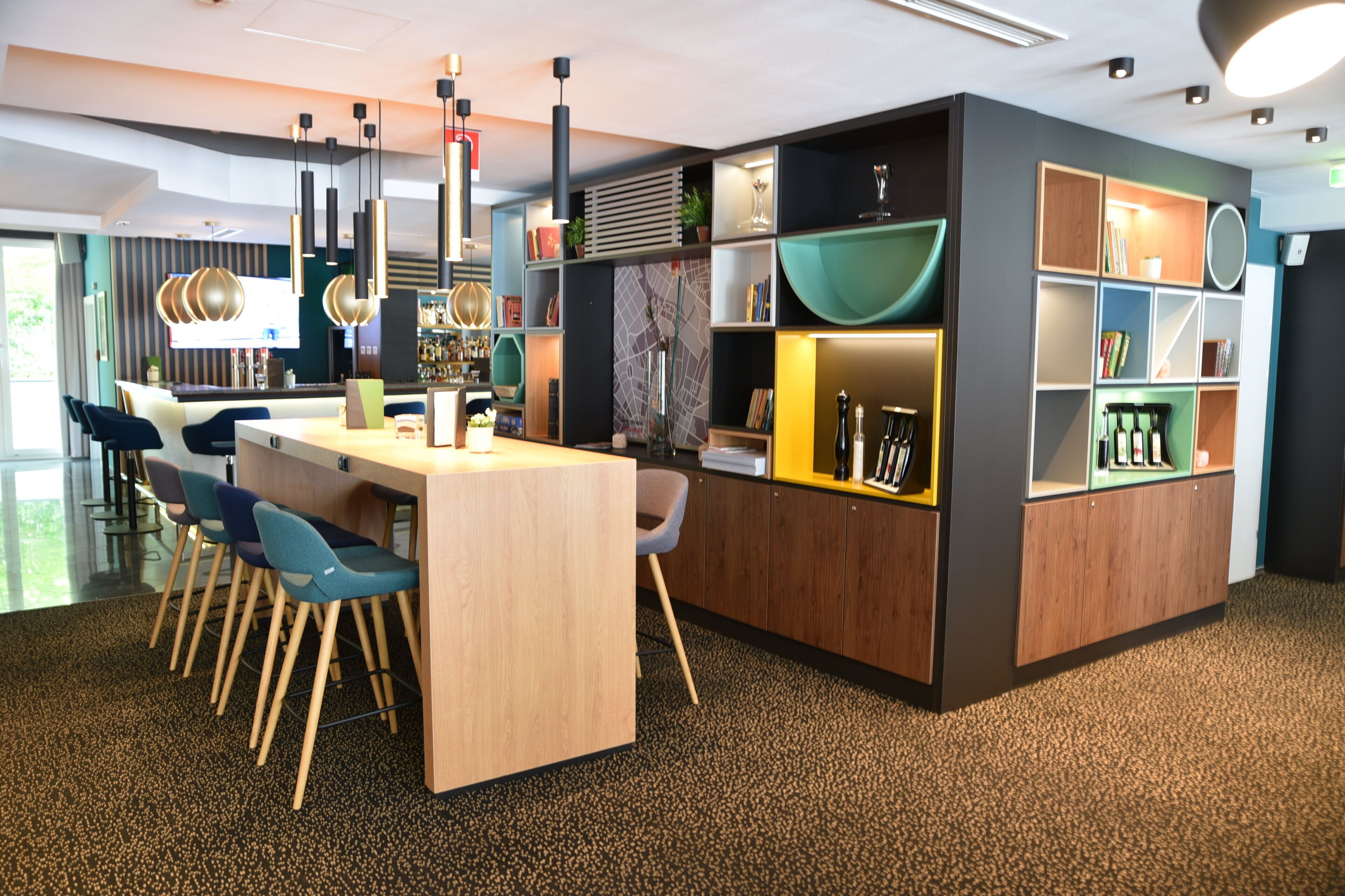 Un intérieur moderne avec un espace de restauration central, un bar et des étagères où sont exposés des livres et des objets décoratifs.