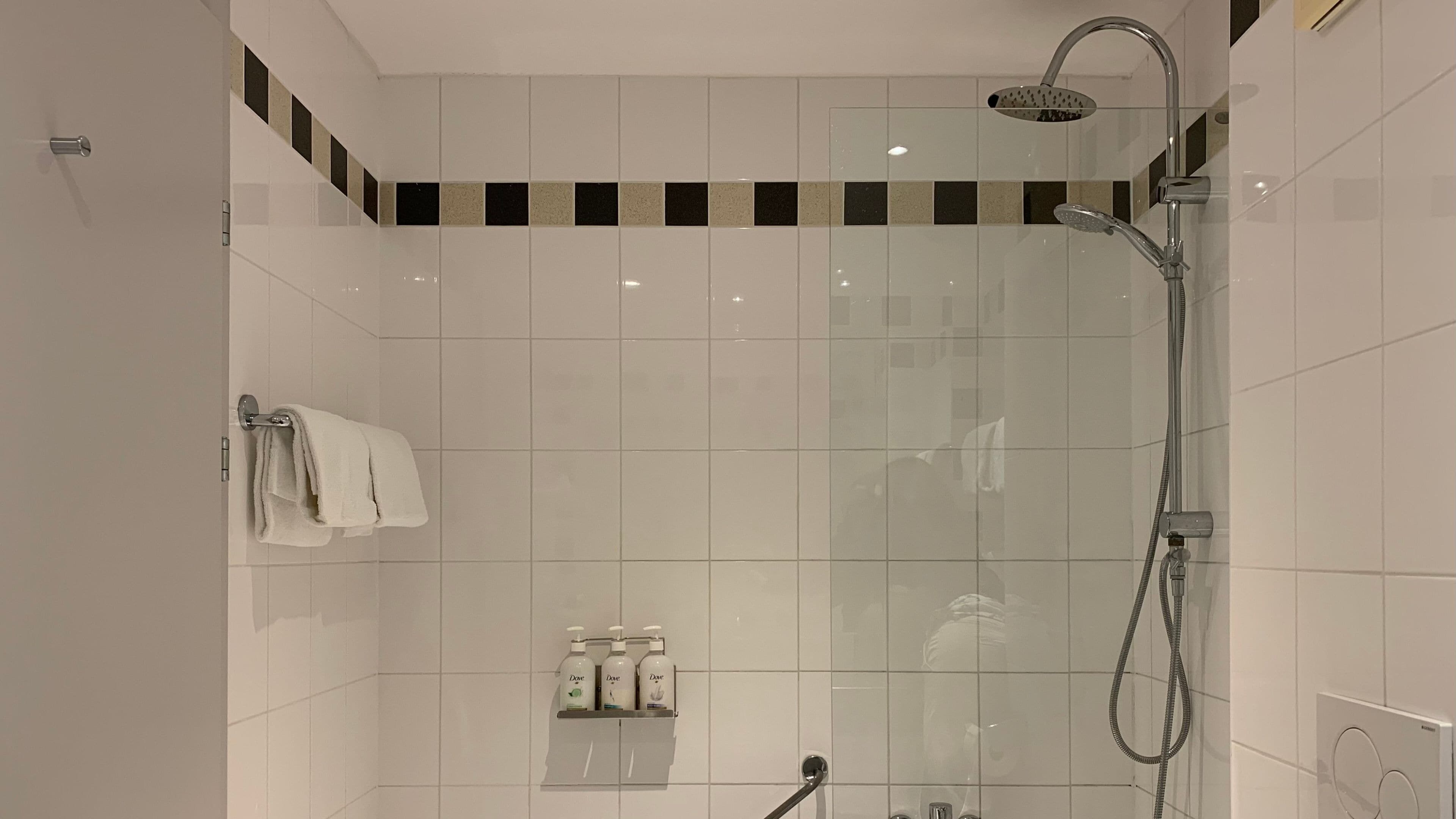A modern shower with a rain showerhead, a handheld showerhead, and a handheld shower attachment.