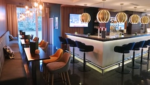 A modern bar area with a bar counter, multiple seating options including bar stools and a sofa, and pendant lighting. - Holiday Inn Salzburg City by IHG (Salzburg)