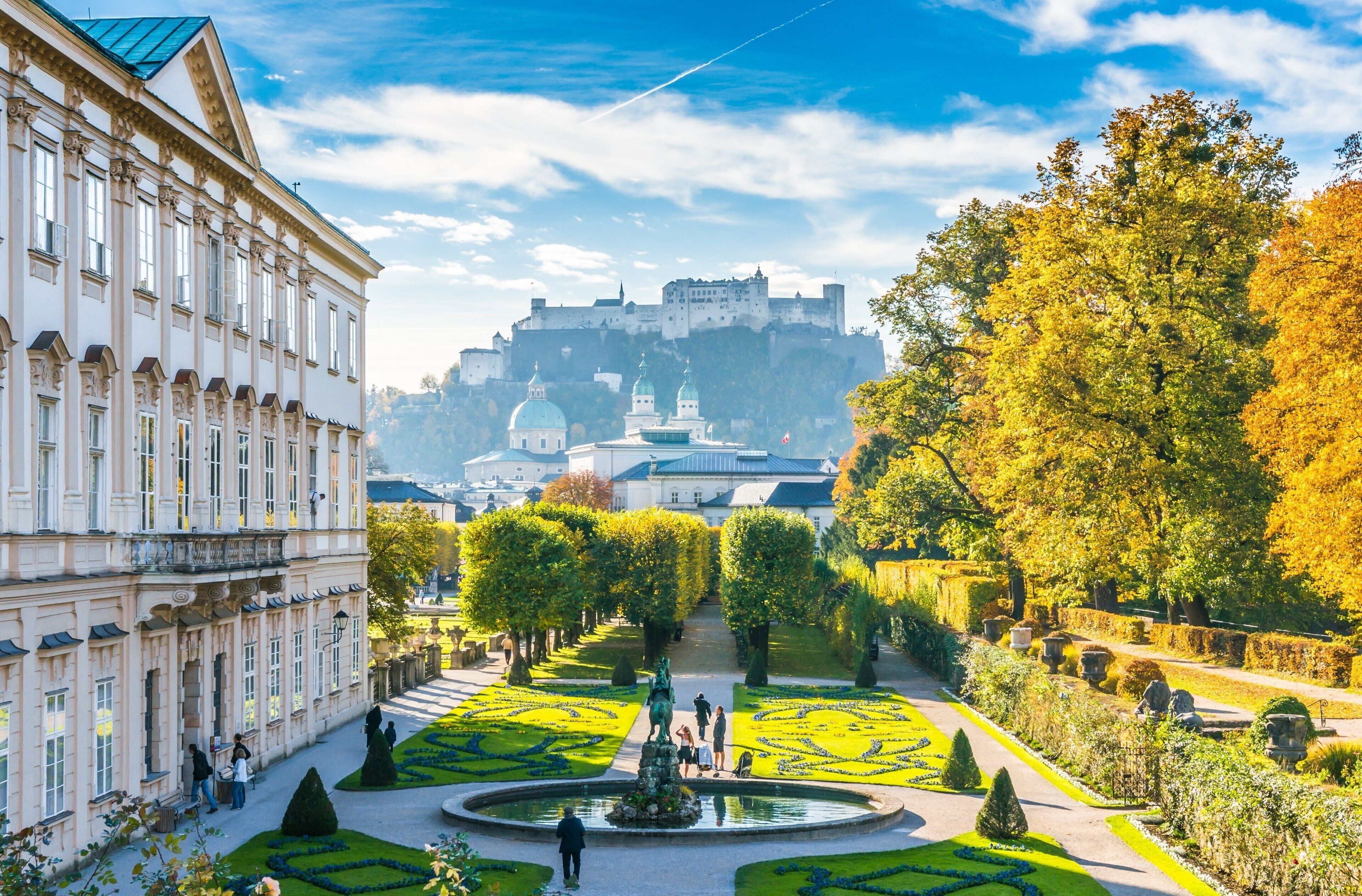 A formal garden with a fountain, manicured lawns, and a large building with classical architecture.